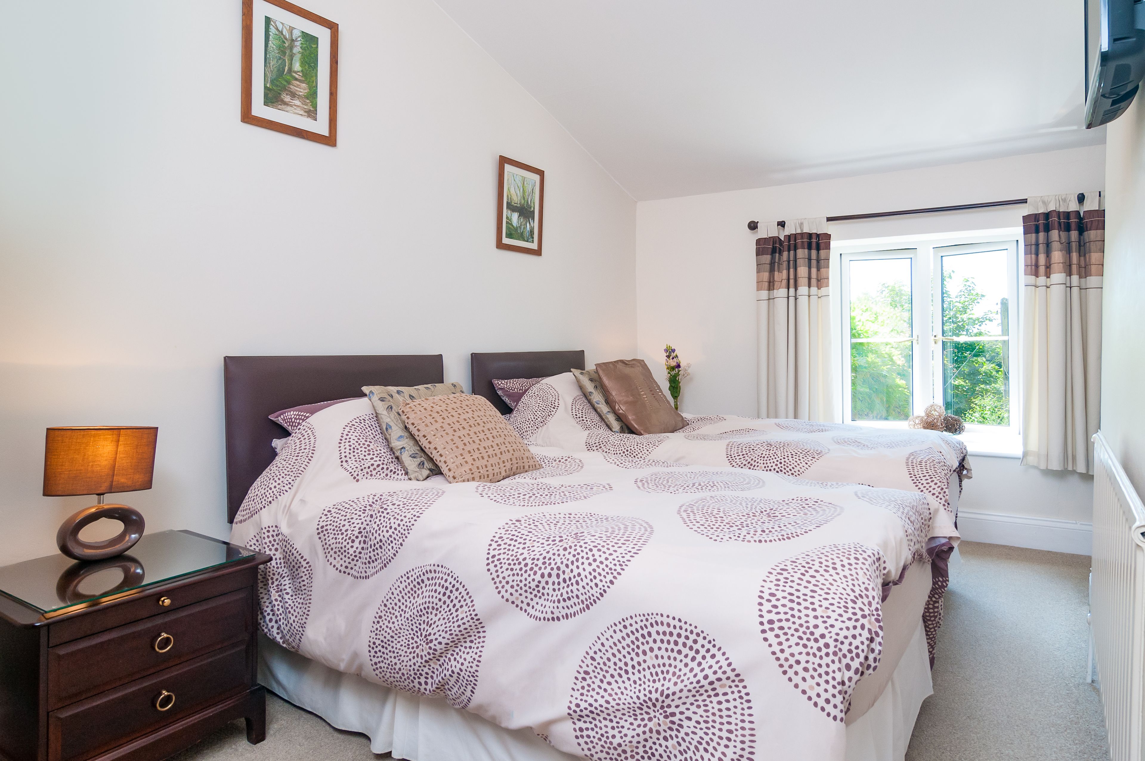 A bedroom with a large bed, a bedside table with a lamp, and two framed pictures on the wall.