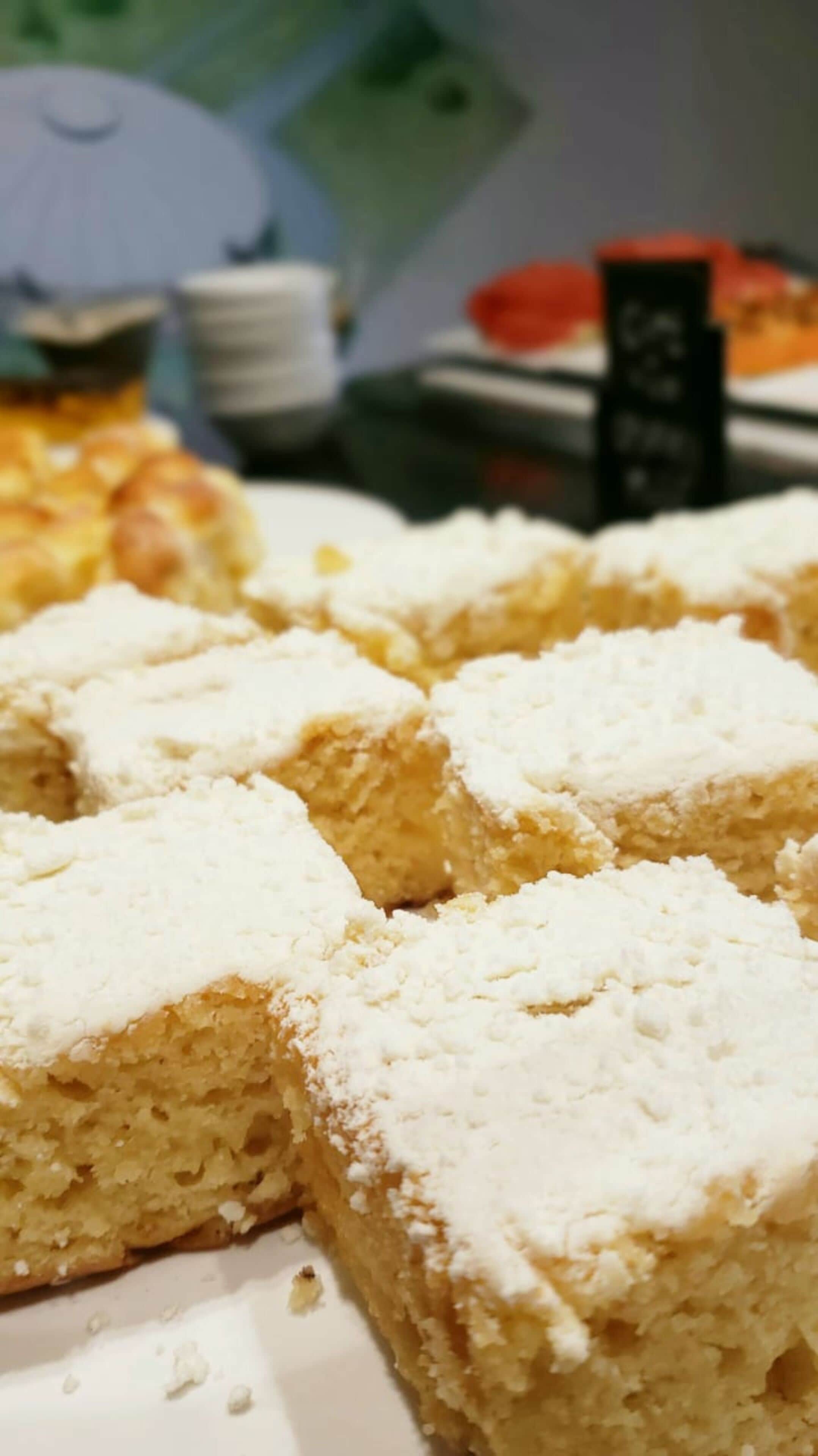 A close-up of a dessert with a powdered topping, possibly a cake or pastry, with a blurred background suggesting a dining setting.