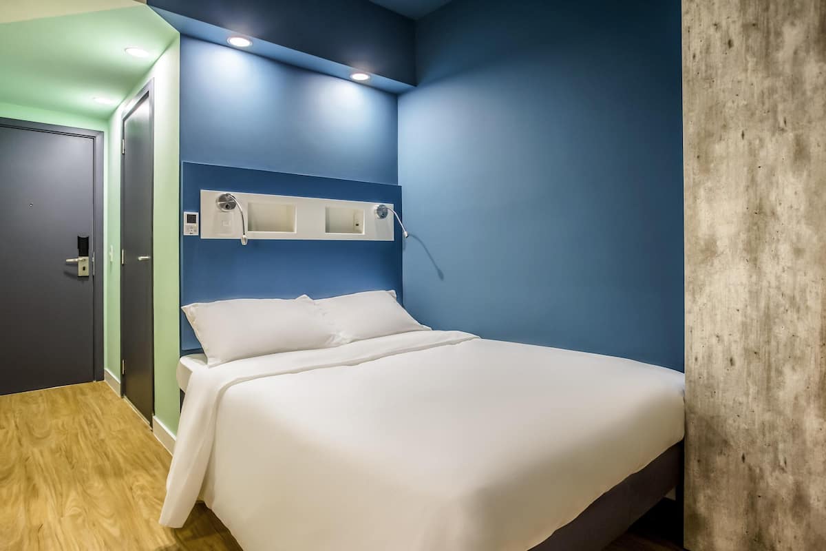 A neatly made bed in a room with a blue accent wall, a wooden floor, and a door with a handle.