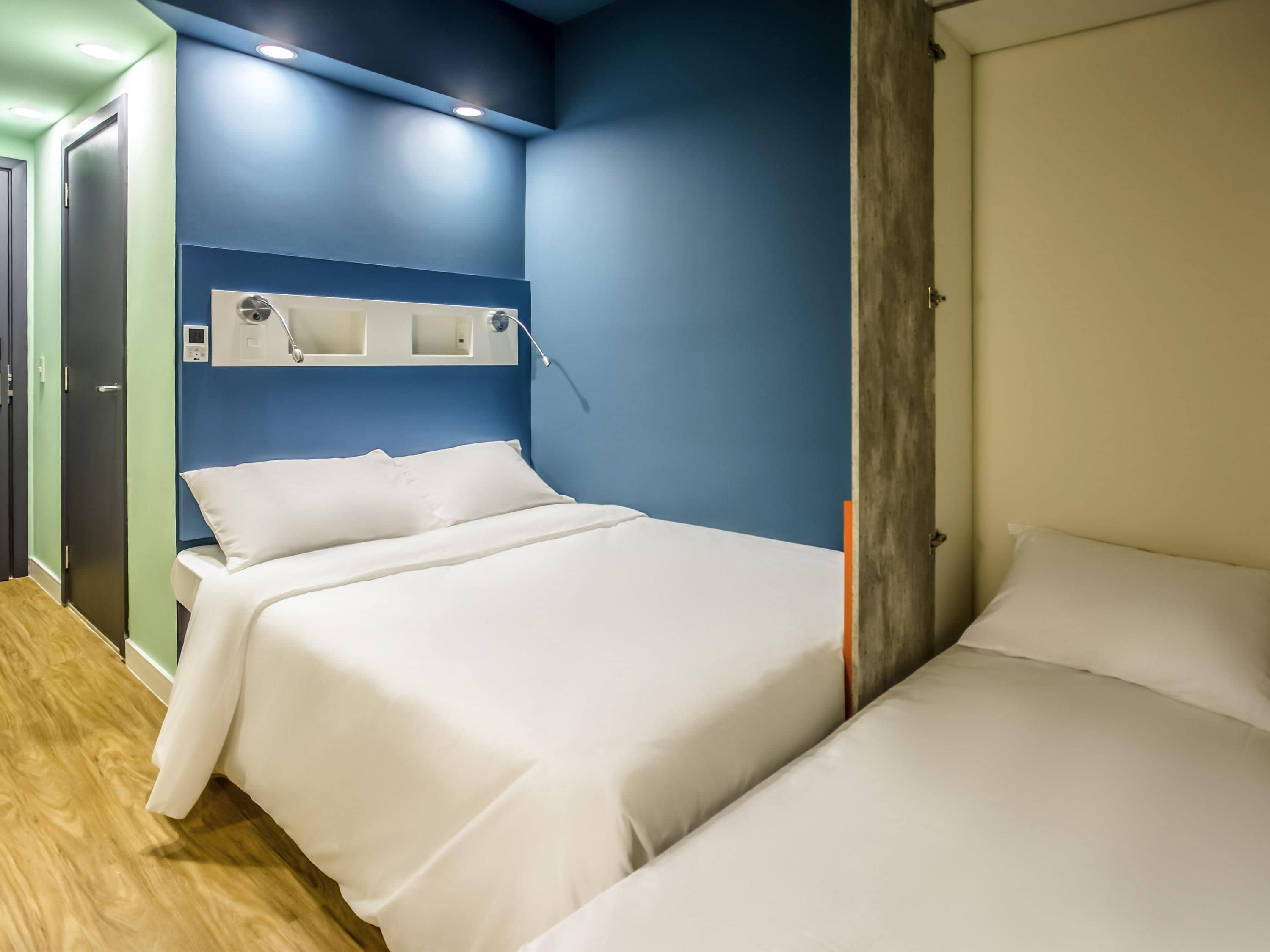 Habitación de hotel con dos camas, suelo de madera, pared azul decorativa y puerta con panel de madera.