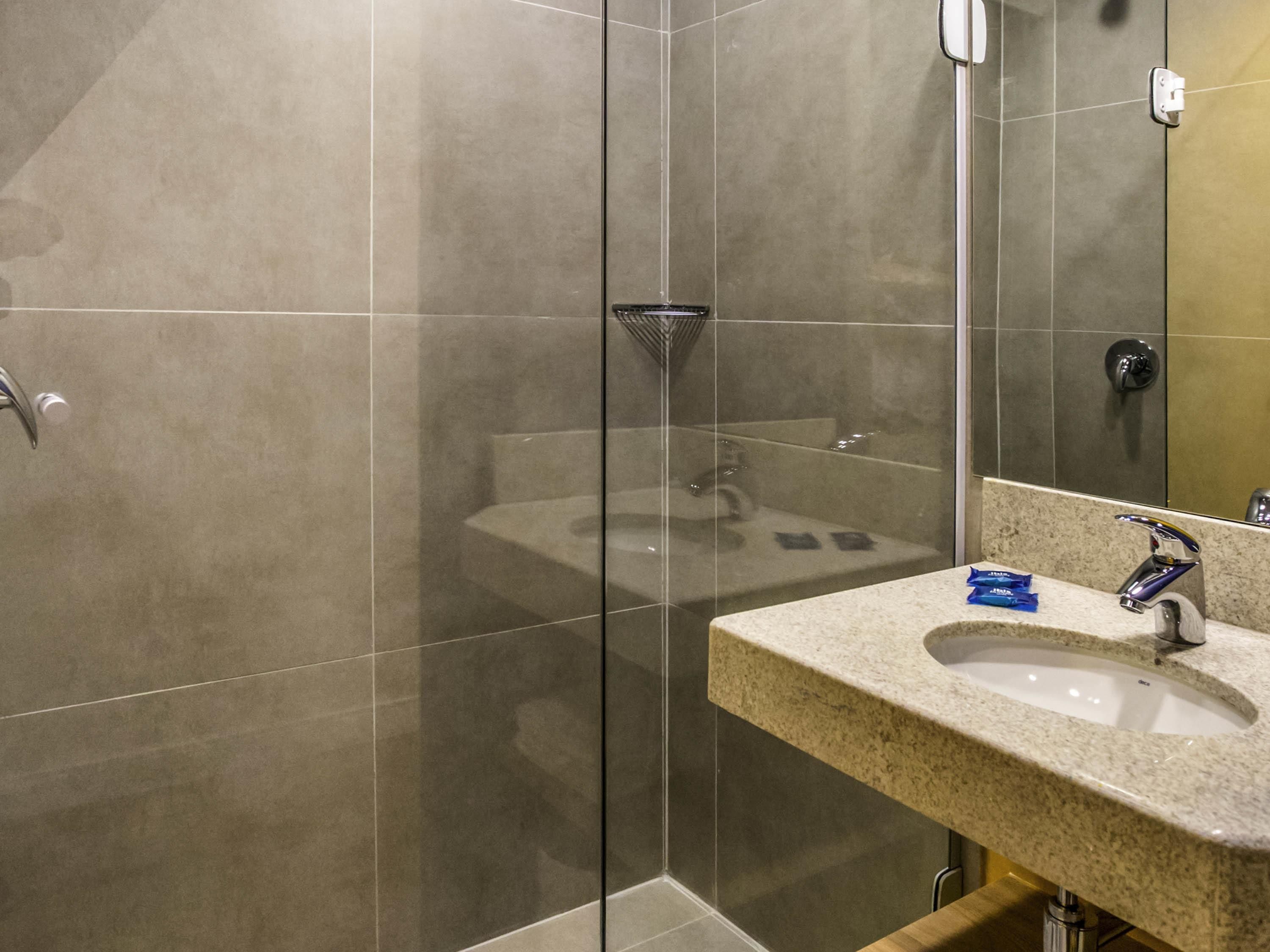 A modern bathroom with a glass shower enclosure, a granite countertop sink, and a large mirror.