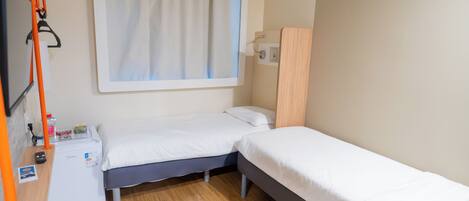 A small, compact room with a single bed, a desk with a computer, and a window with curtains.