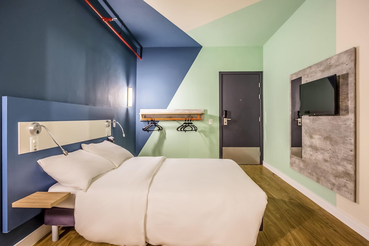Une chambre d’hôtel moderne équipée d’un lit, d’une table de chevet et d’un téléviseur fixé au mur.
