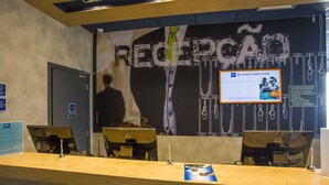 Una mesa de recepción con mostrador de madera, dos sillas y un ordenador Dell. Un cartel con la palabra “RECLIPCAO” está en la pared.