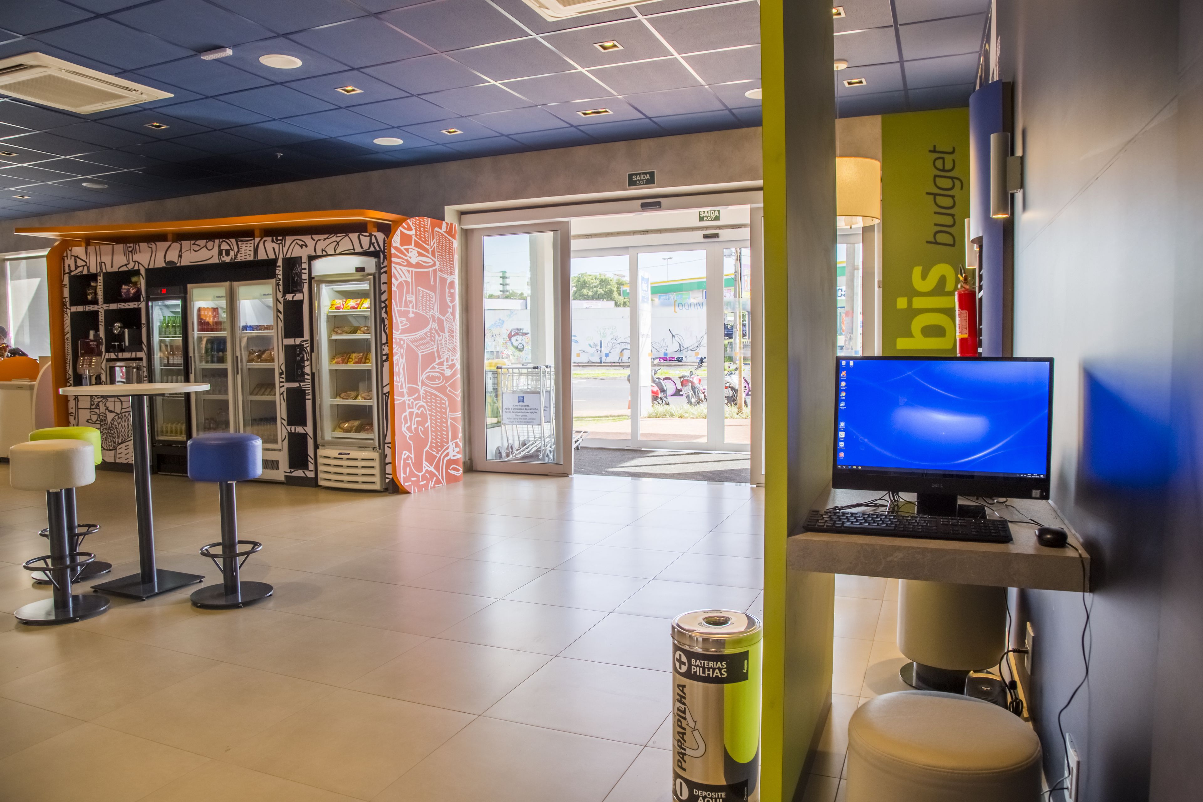 A modern interior with a computer desk, a vending machine, and a seating area with stools.