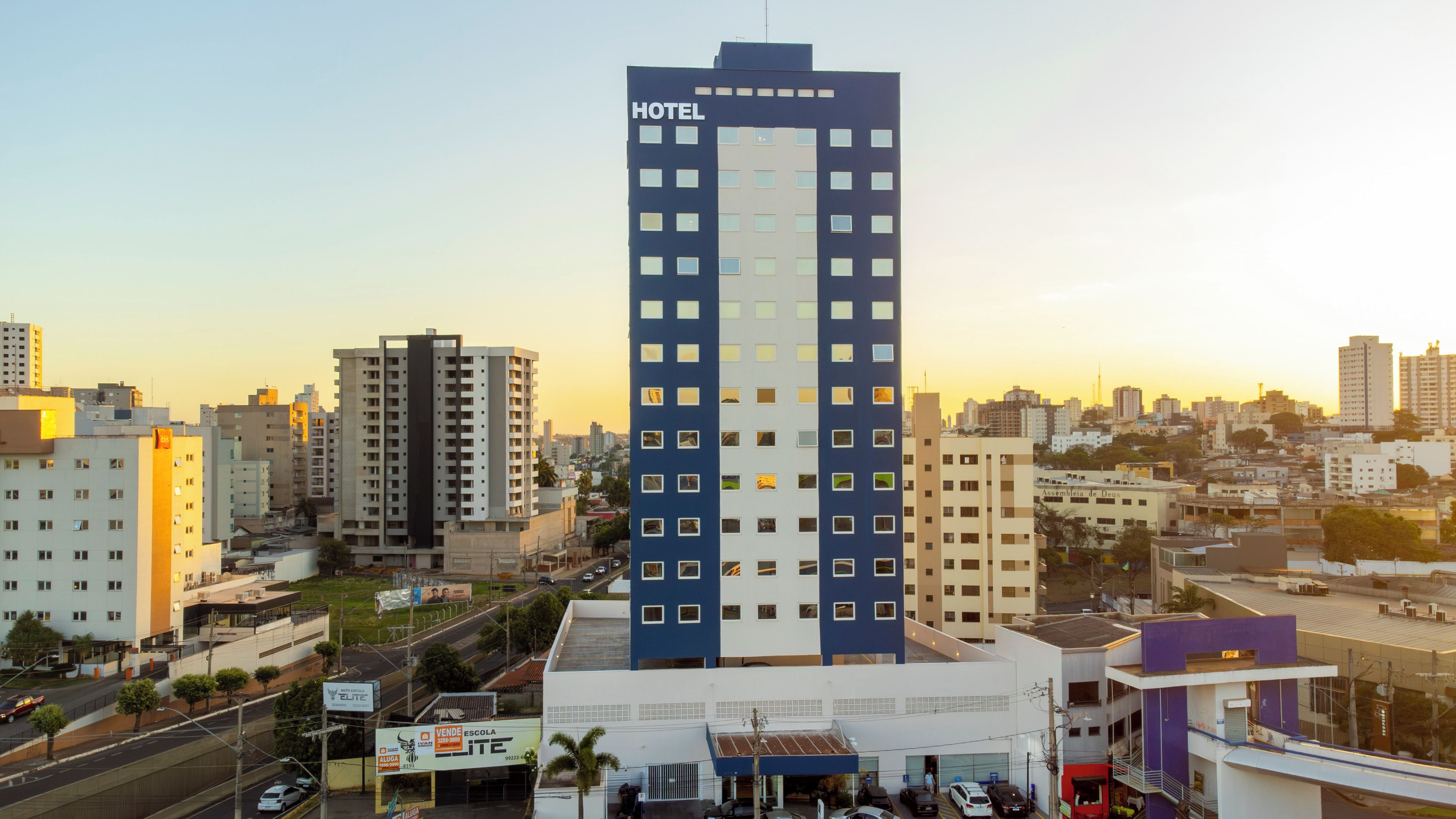 Um hotel com vários andares e um grande letreiro 'HOTEL', em meio a outros edifícios em uma paisagem urbana.