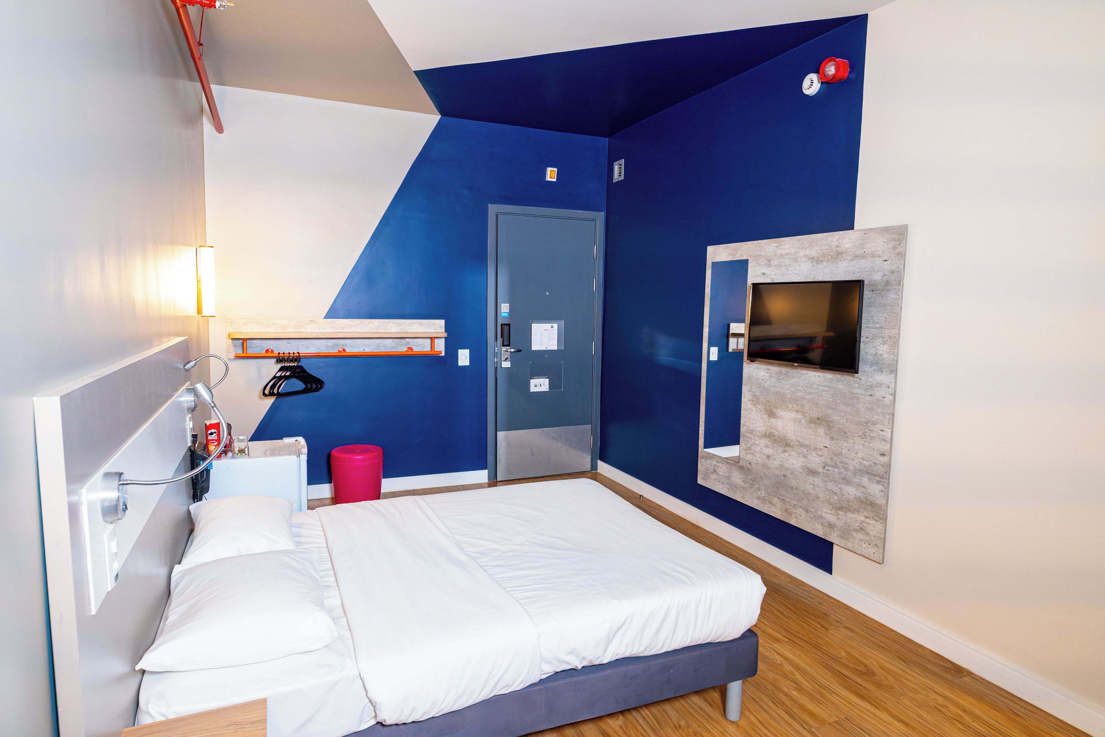 A modern hotel room with a bed, a desk, a TV, and a door.