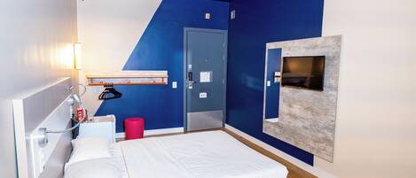 A modern hotel room with a bed, a desk, a TV, and a door.