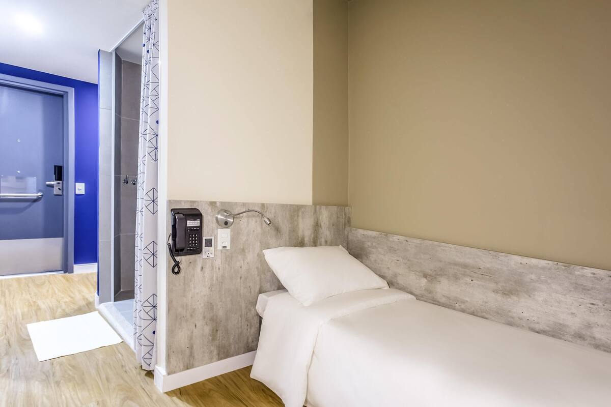 A hotel room with a bed, a phone, and a shower area.