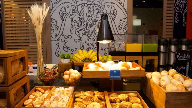 Un bufé de desayuno con diversos pasteles y frutas, una pared decorativa con diseños abstractos y una lámpara negra.