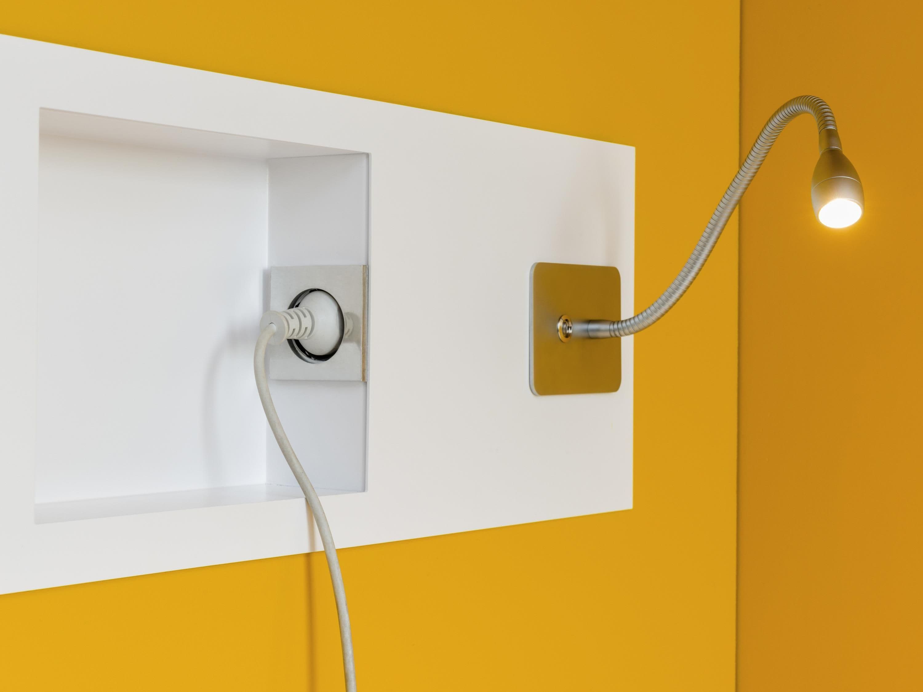 A bathroom with a white wall, a yellow accent wall, a showerhead, and a light fixture.