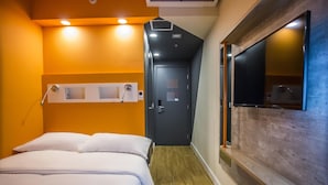 Habitación de hotel con una cama, suelo de madera, un televisor montado en la pared y una puerta que da a otra habitación.