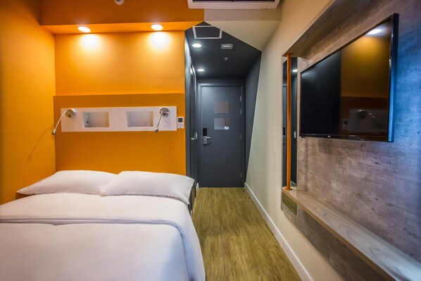 A hotel room with a bed, a wooden floor, a TV mounted on the wall, and a door leading to another room.