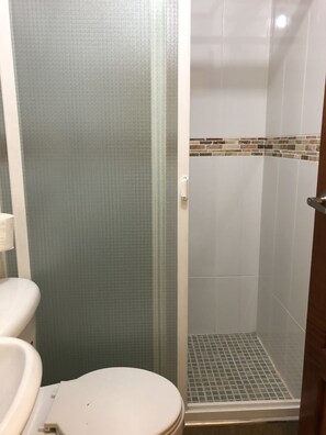 A bathroom with a toilet, a shower with a tiled floor, and a wall with a textured pattern. - Casa Hotel la Casa Vieja (San Salvador)
