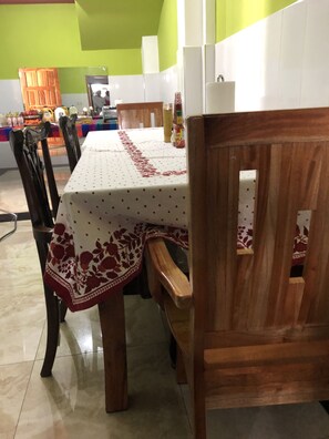 A dining area with a table covered by a white tablecloth with red floral patterns, surrounded by wooden chairs. - Casa Hotel la Casa Vieja (San Salvador)
