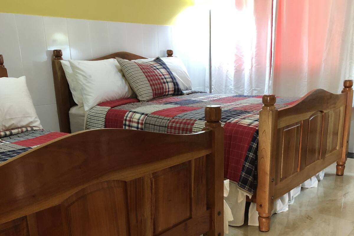 Ein Schlafzimmer mit zwei hölzernen Betten, einem Fliesenboden und einem Fenster mit Vorhängen.