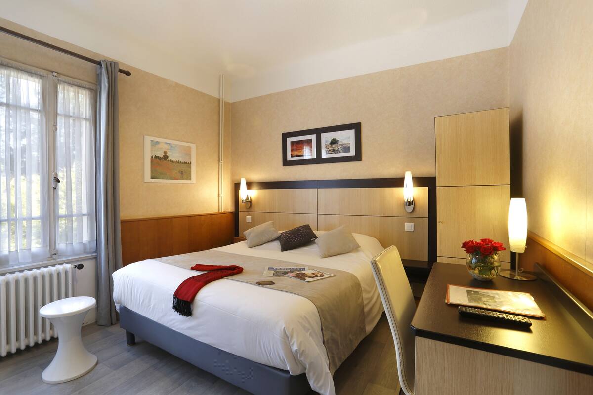 A hotel room with a bed, bedside table, lamp, and a window with curtains.