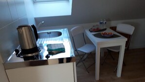 Una pequeña kitchenette con un lavabo, una tetera y una mesa con sillas.