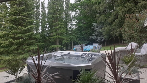 Un jacuzzi rodeado de plantas en macetas y mobiliario de exterior.
