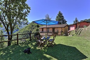 A rustic outdoor seating area with a table and chairs under a blue umbrella, surrounded by a wooden fence and a grassy lawn, with a mountain view in the background. - Agriturismo Le Scope (Molazzana)