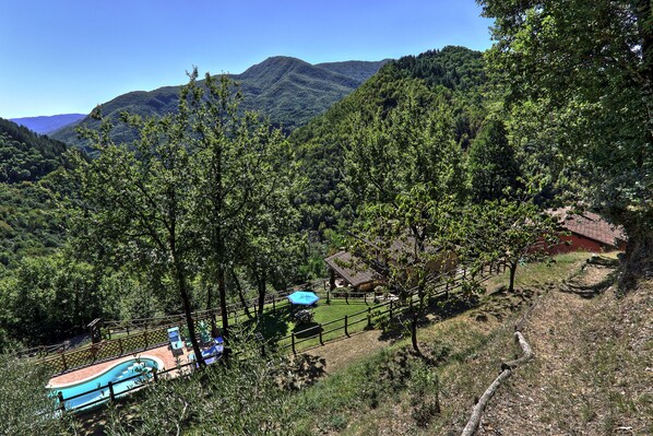A mountainous landscape with a fenced swimming area, a small building, and a wooden path.