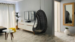 A modern living room with a hanging chair, a flat-screen TV, a sofa, and a dining area with a small table and chairs.