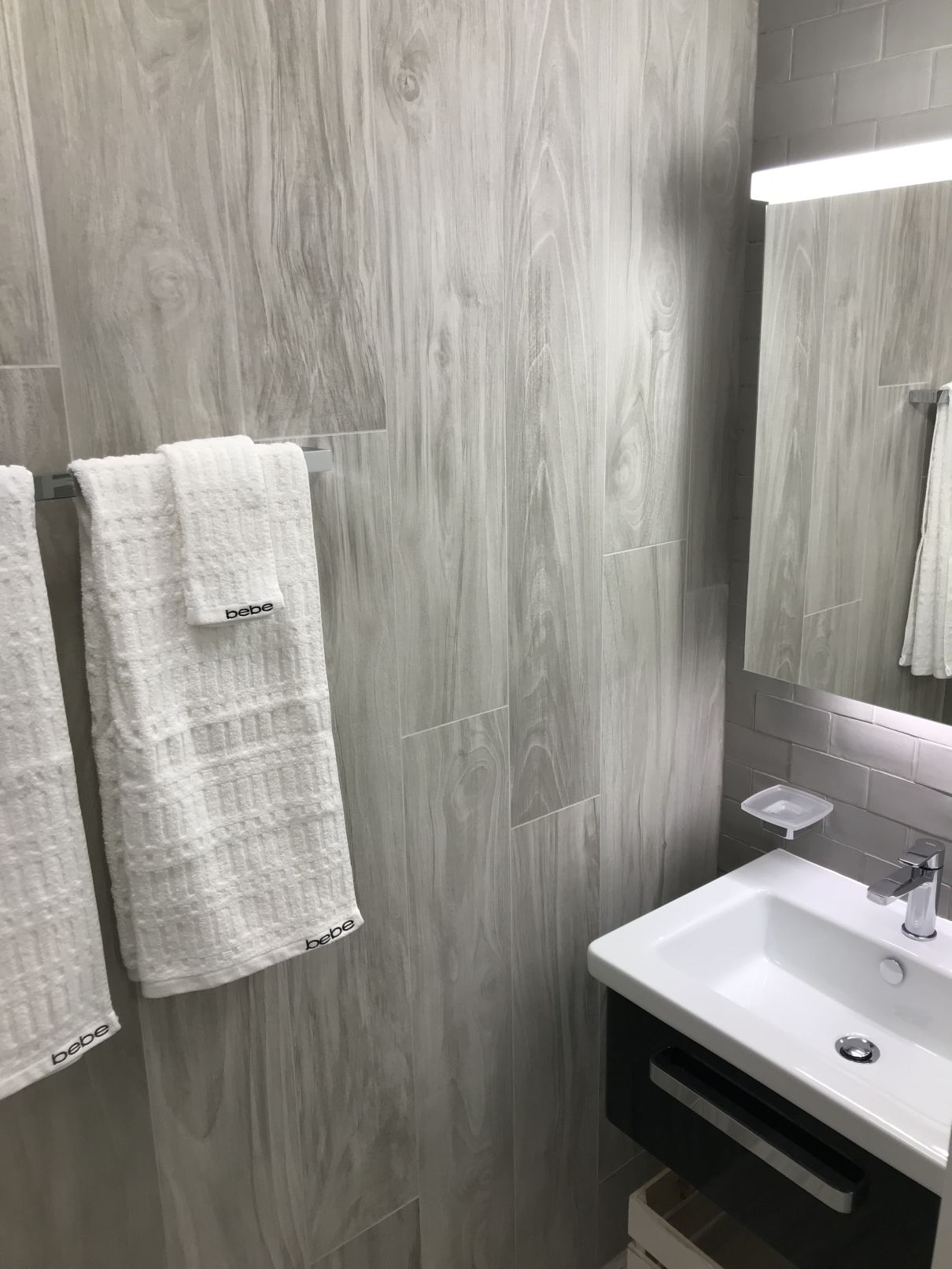 A bathroom with a wooden wall, a white sink, and two white towels hanging on hooks.