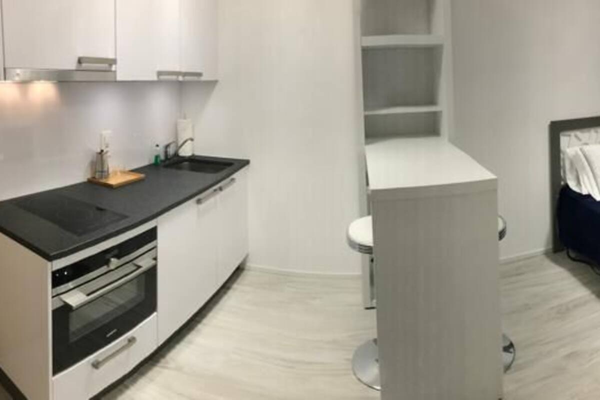 A compact room with a kitchenette, a bed with a blue blanket, and a TV mounted on the wall.