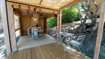 Eine Holzterrasse mit Tisch und Stühlen, einer kleinen Küchenzeile und Blick auf eine felsige Landschaft mit Bäumen.
