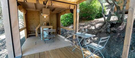Una terraza de madera con mesa y sillas, una kitchenette pequeña, y vistas a un paisaje rocoso con árboles.