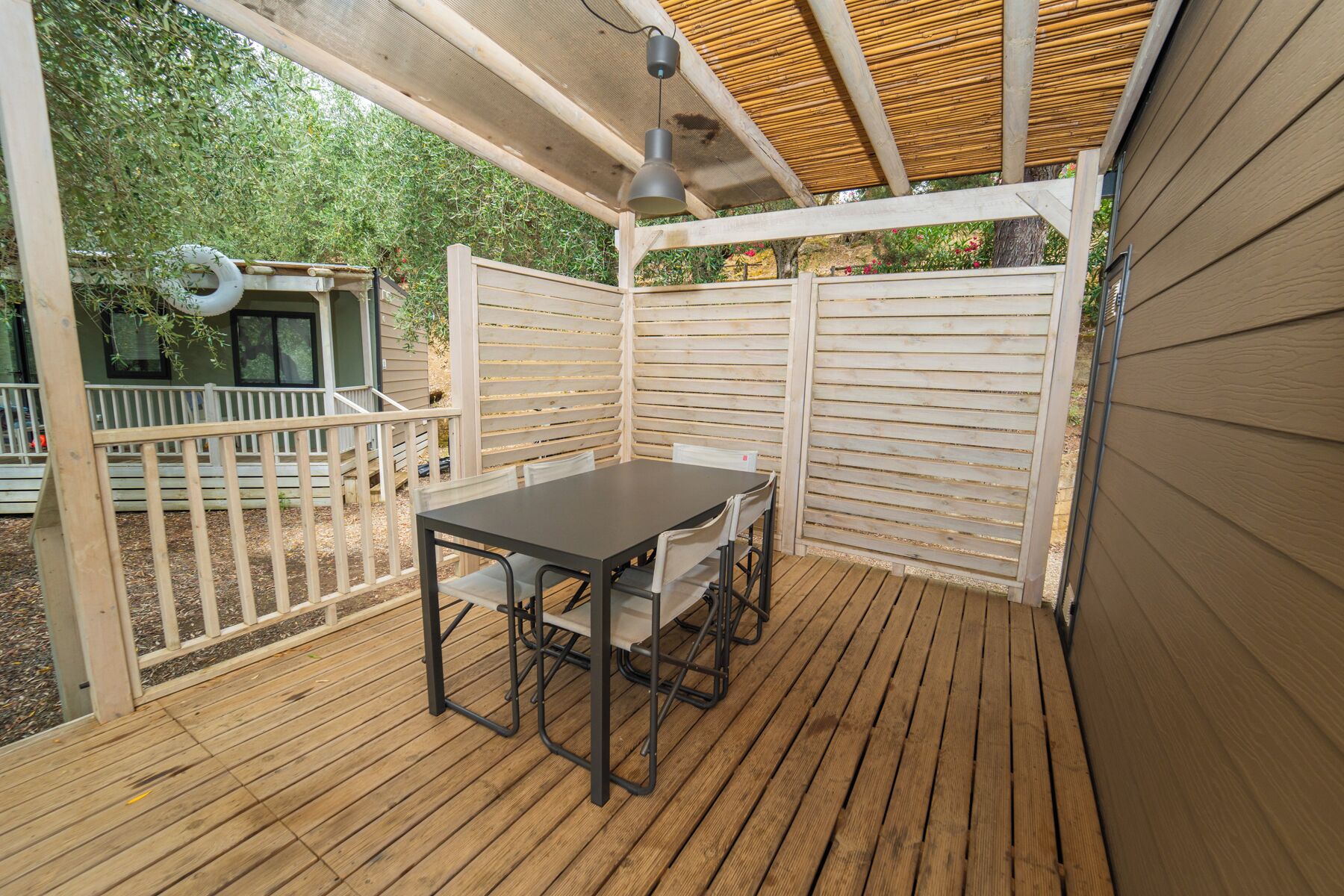 En overdækket terrasse med et bord og stole, træterrasse og et hvidt hegn.