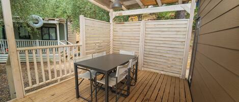 En overdækket terrasse med et bord og stole, træterrasse og et hvidt hegn.