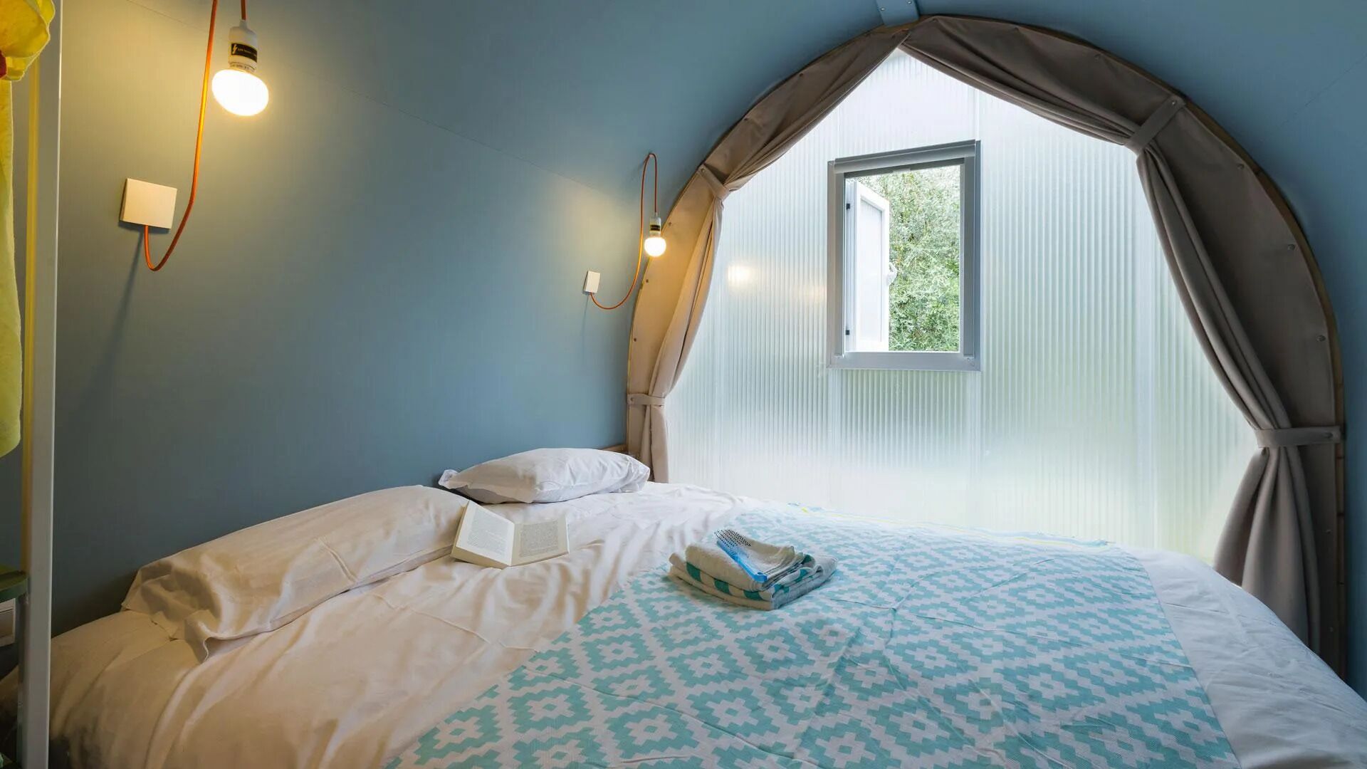 A bedroom with a bed, a window with curtains, and wall-mounted lights.