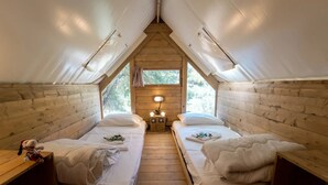 Un hébergement confortable en forme de tente, doté de deux lits, d’une petite table avec une lampe et offrant une vue sur la verdure environnante.