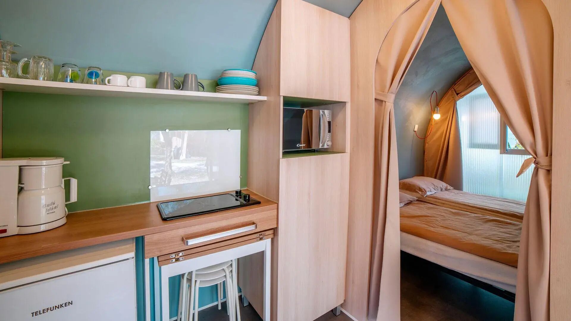 A compact bedroom with a bed, a small desk, a coffee maker, and a TV.