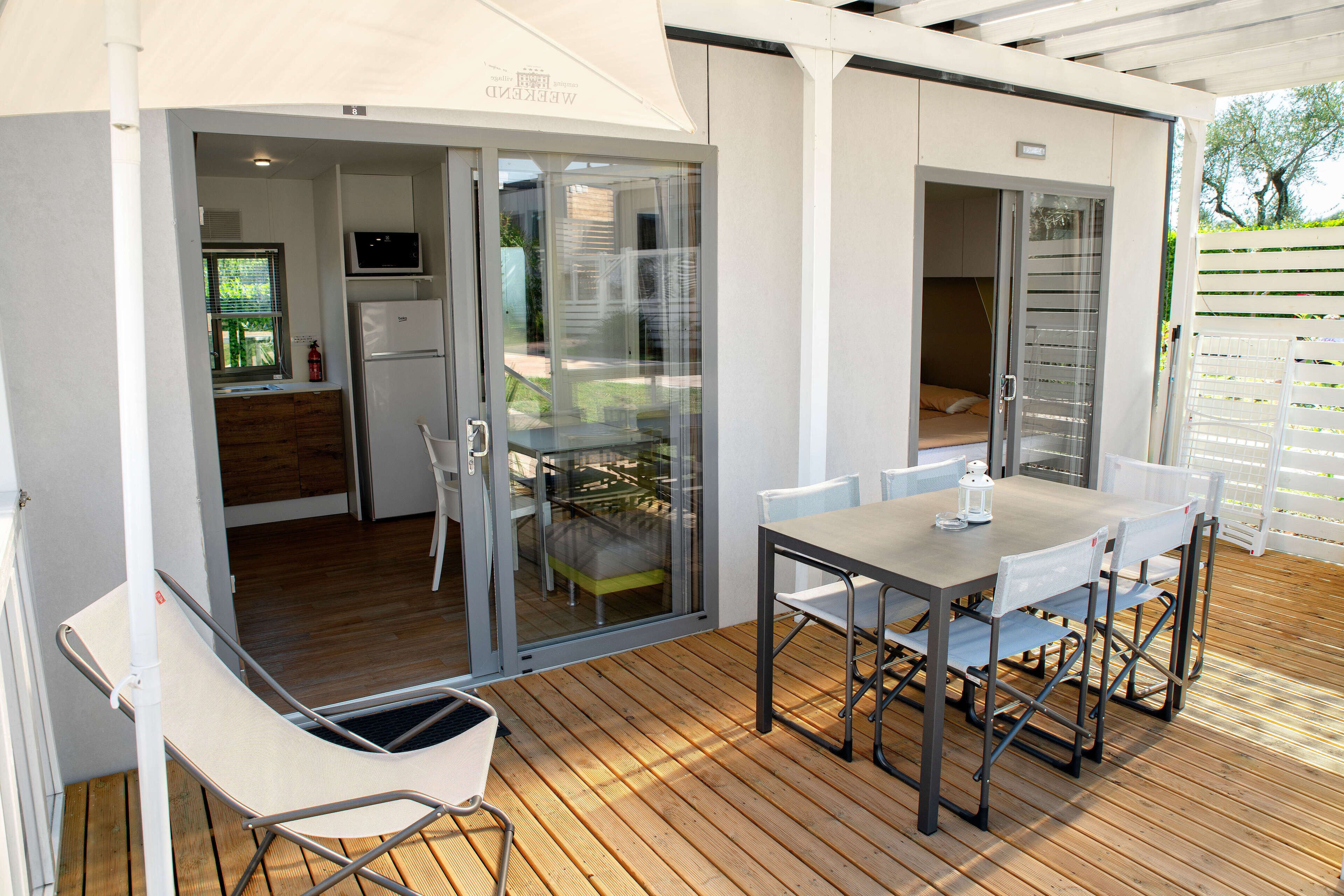 Eine moderne Terrassengruppe mit Holzboden, einem Tisch mit Stühlen und einer Glastür, die in einen Küchenbereich führt.