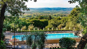 Un espace piscine agrémenté de chaises longues et de parasols, entouré d’arbres et offrant une vue sur des collines lointaines.