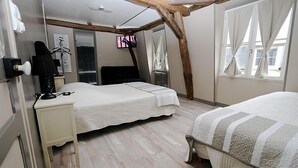 A bedroom with a bed, a desk, a chair, a TV, and a window with curtains.