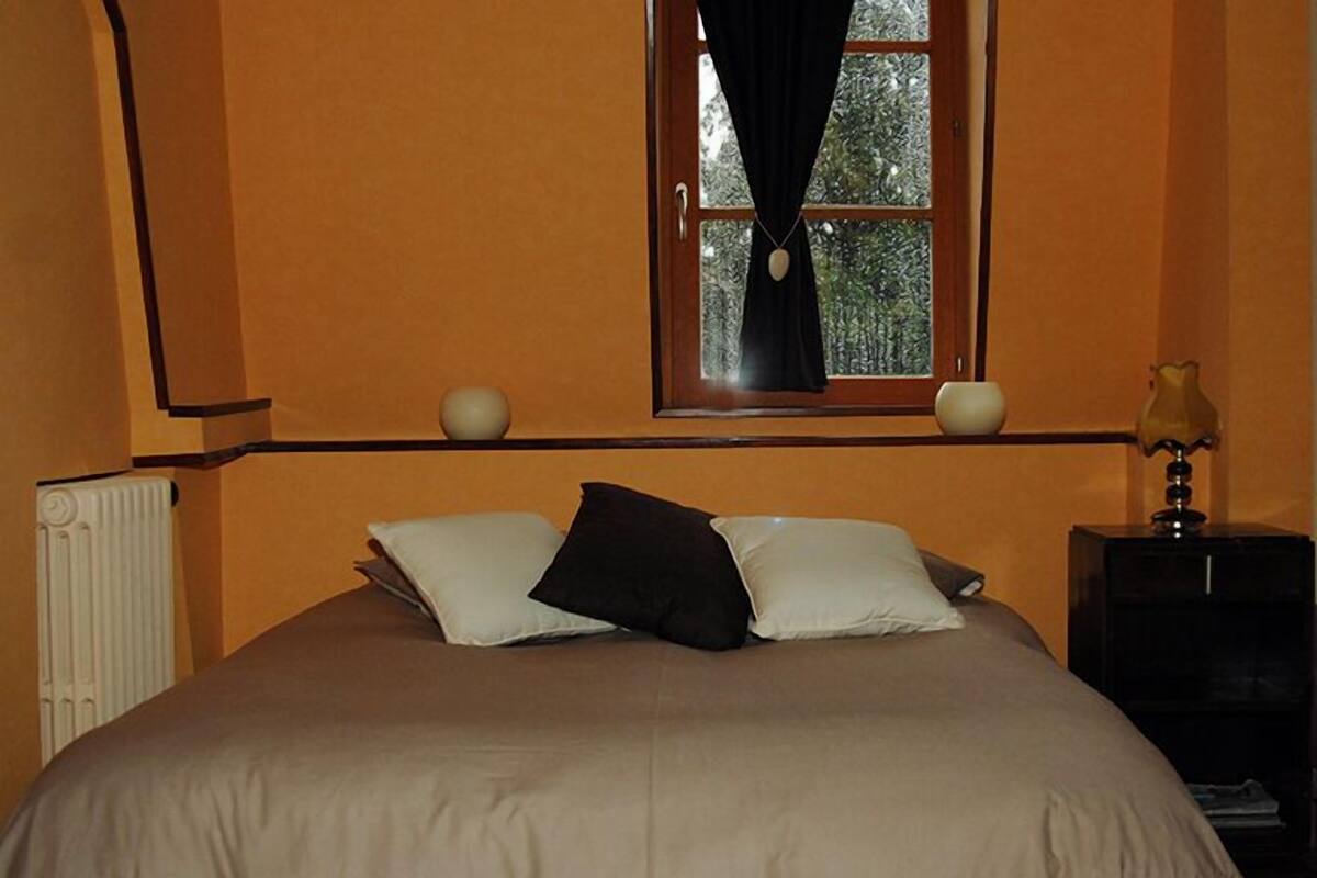 Un dormitorio con cama, ventana con cortinas, mesita de noche y lámpara.
