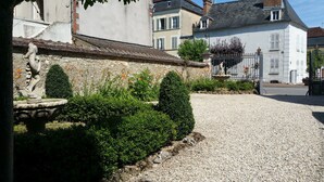 A courtyard with a gravel path, a stone fountain, and neatly trimmed hedges.