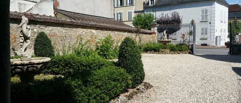 A courtyard with a gravel path, a stone fountain, and neatly trimmed hedges.
