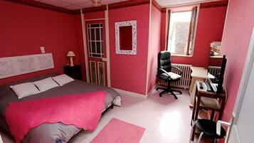 A bedroom with a bed, a desk, a chair, a radiator, and a window.