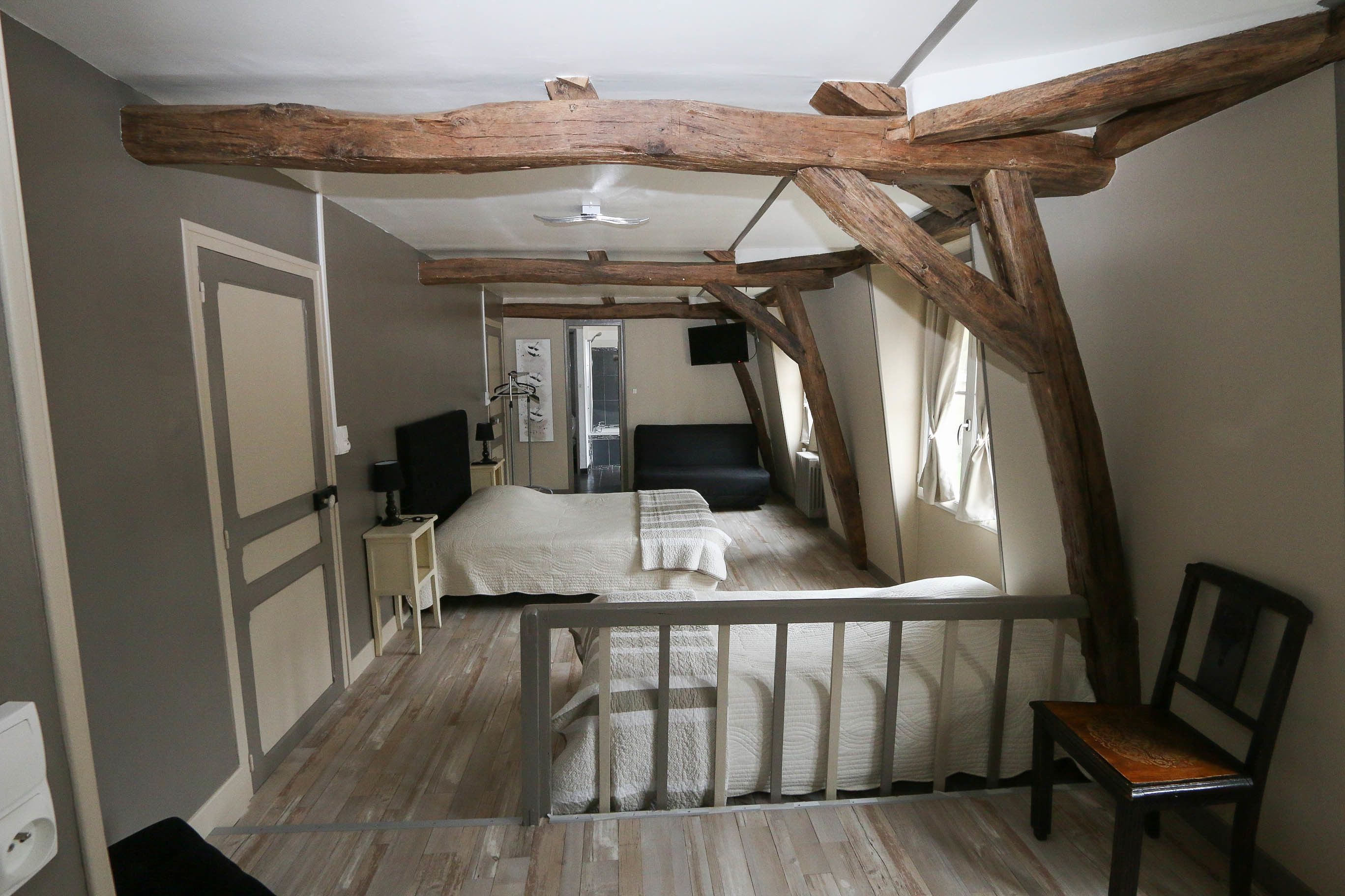 A bedroom with a wooden ceiling, a bed with a white mattress, a nightstand, a chair, and a window with curtains.