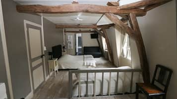 Un dormitorio con techo de madera, una cama con colchón blanco, una mesita de noche, una silla y una ventana con cortinas.