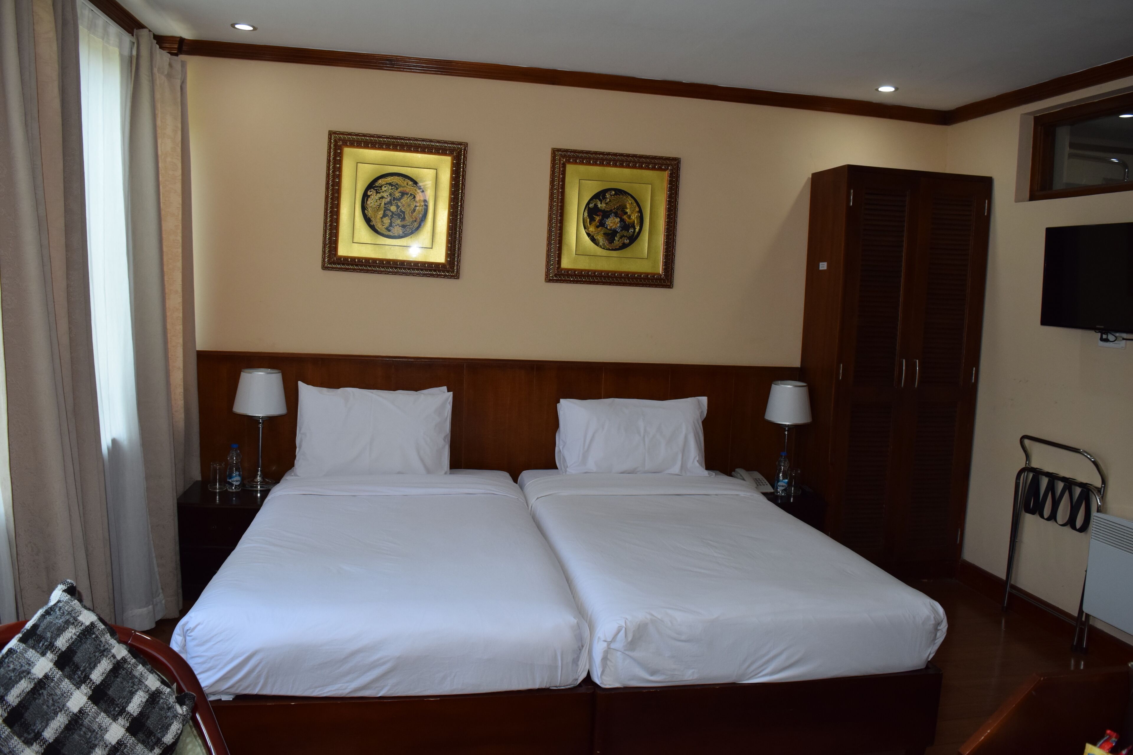 A hotel room with two beds, a wardrobe, a television, and two framed pictures on the wall.