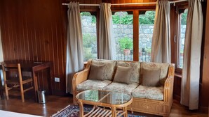 A cozy room with a wooden sofa, a glass coffee table, and a wicker chair. - Kisa Villa (Thimphu)