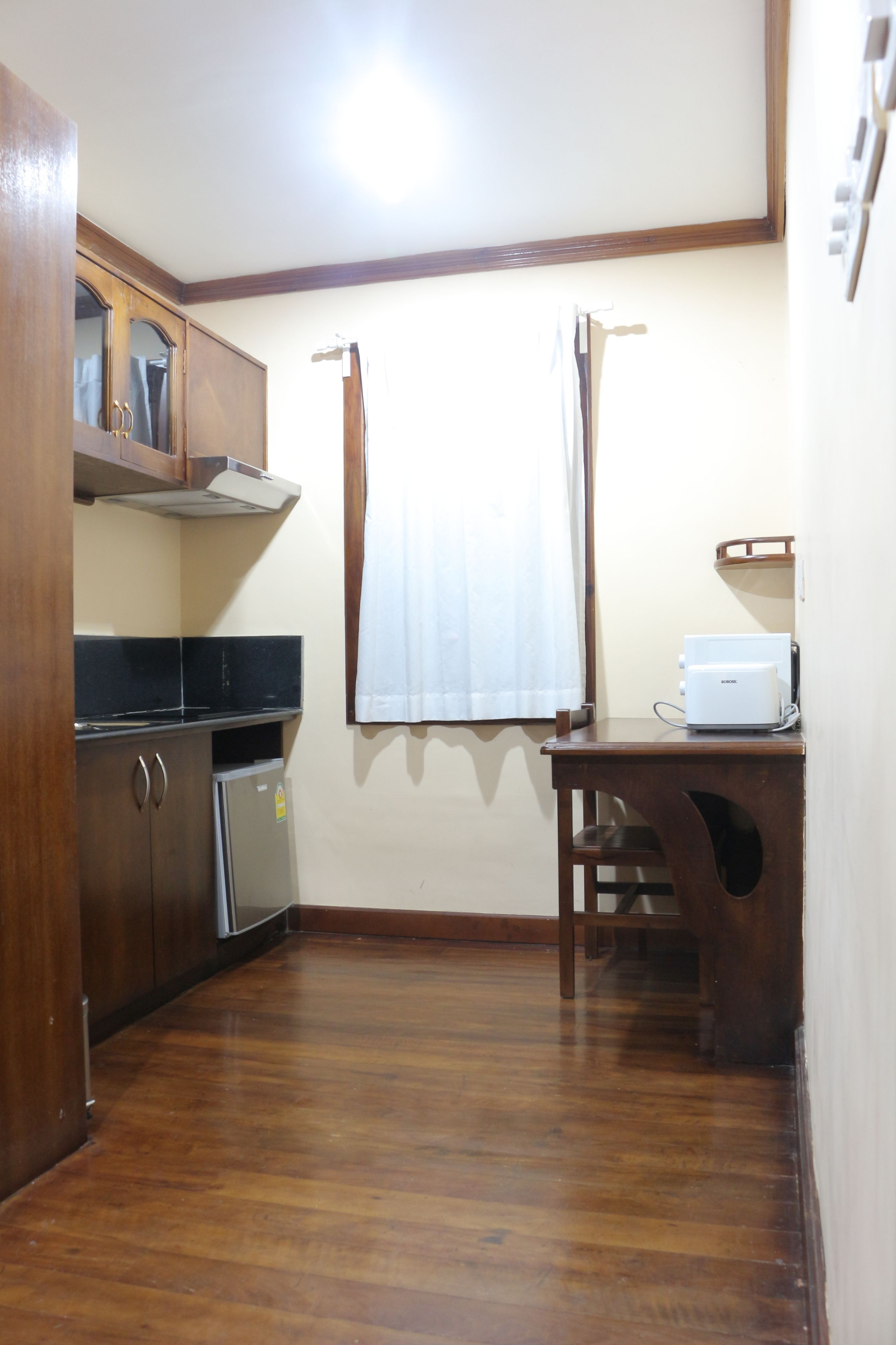 Una cocina con armarios de madera, un refrigerador, una encimera y una ventana con cortinas.