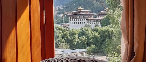 A room with a wicker bed, a view of a mountain and a building through an open door.