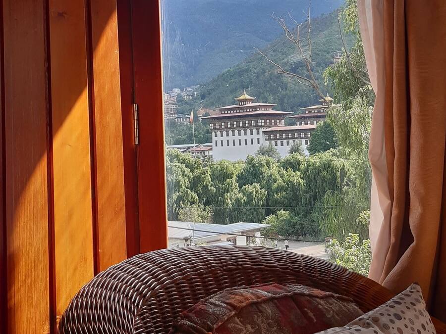 A room with a wicker bed, a view of a mountain and a building through an open door.