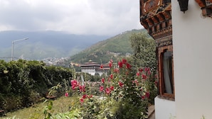 A traditional building with ornate architecture, a garden with pink flowers, and a mountainous backdrop. - Kisa Villa (Thimphu)